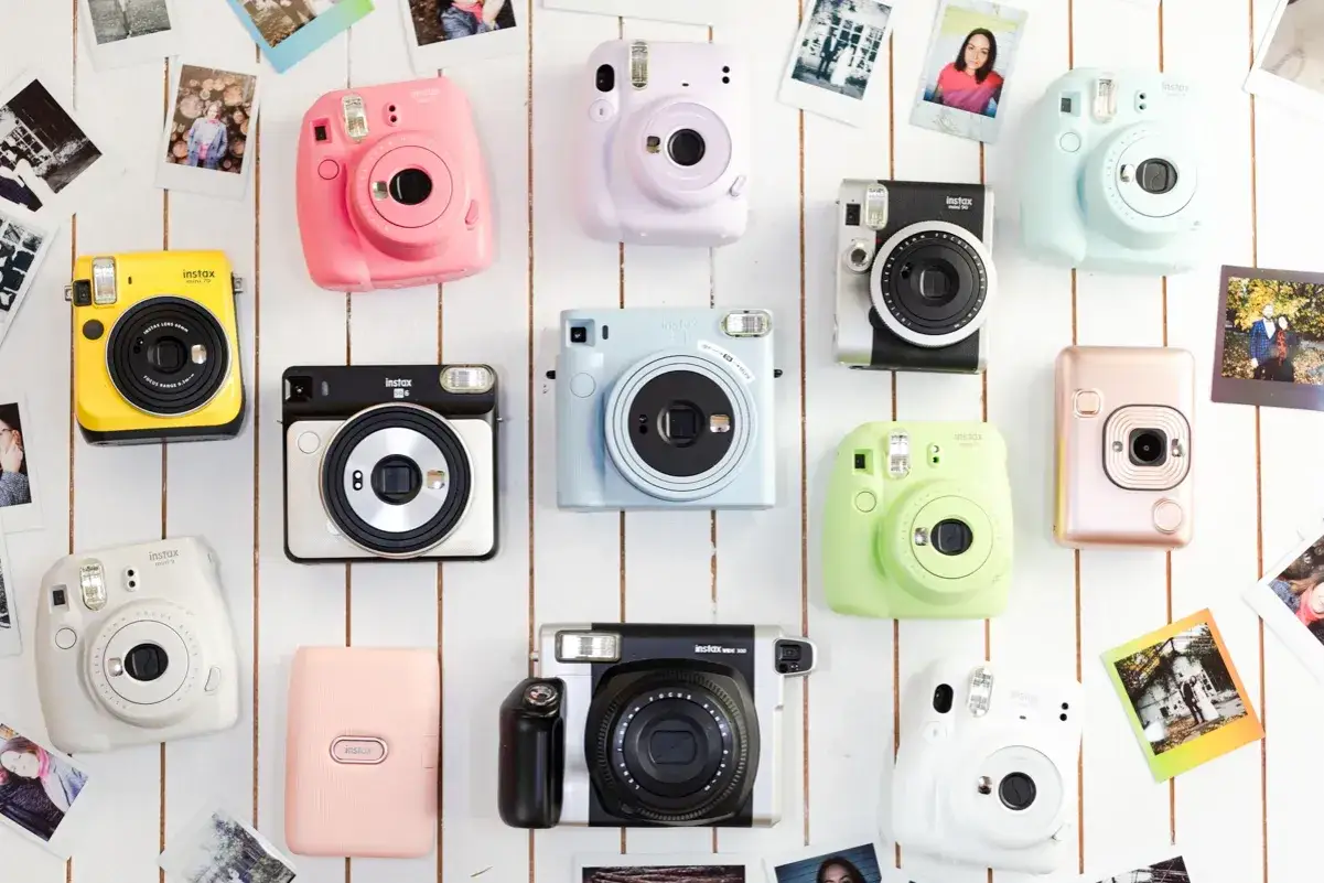 Kolekcja kolorowych aparatów Instax, jakby widziana przez wizjer kamery. Obraz zawiera żółty, różowy, fioletowy, niebieski, zielony, biały i różowo-złoty aparat.