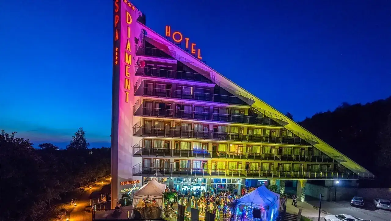 Hotel Diament Wisła nocą, rozświetlony neonami. Na dole odbywa się impreza plenerowa.