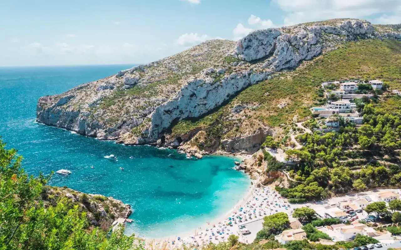 Bahía turquesa con arena blanca, una de las mejores playas de Alicante, rodeada de acantilados y vegetación.