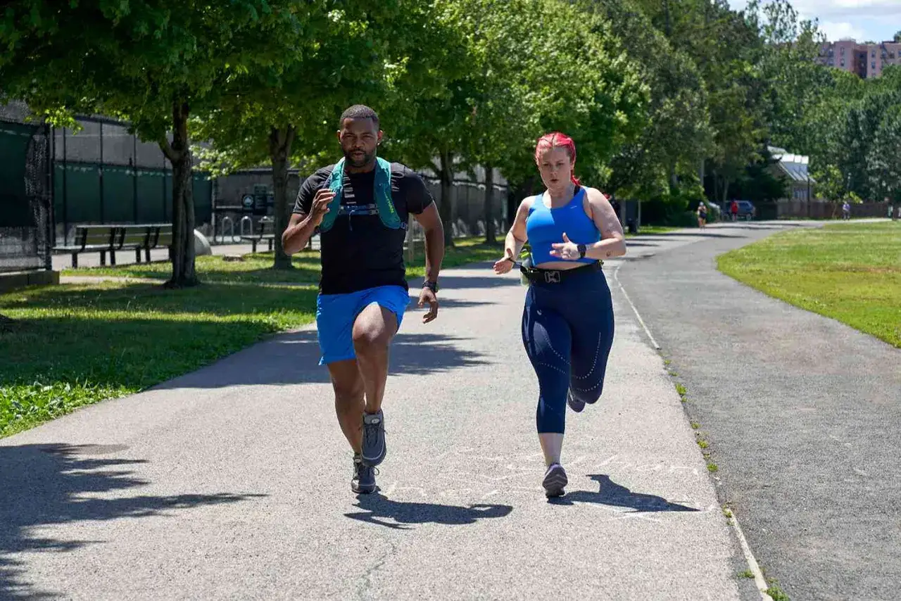 Para biegnie ścieżką w parku. Ona w niebieskim sportowym topie i legginsach, on w czarnej koszulce i niebieskich spodenkach. To inspiracja dla bieganie dla otyłych.