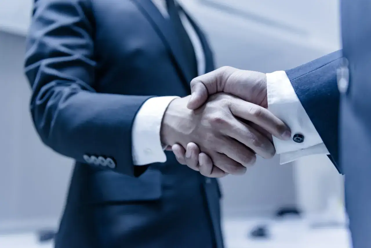 Dwóch mężczyzn w garniturach ściska sobie dłonie, symbolizując zawarcie umowy lub partnerstwa. To kluczowy moment dla ich spółki partnerskiej.