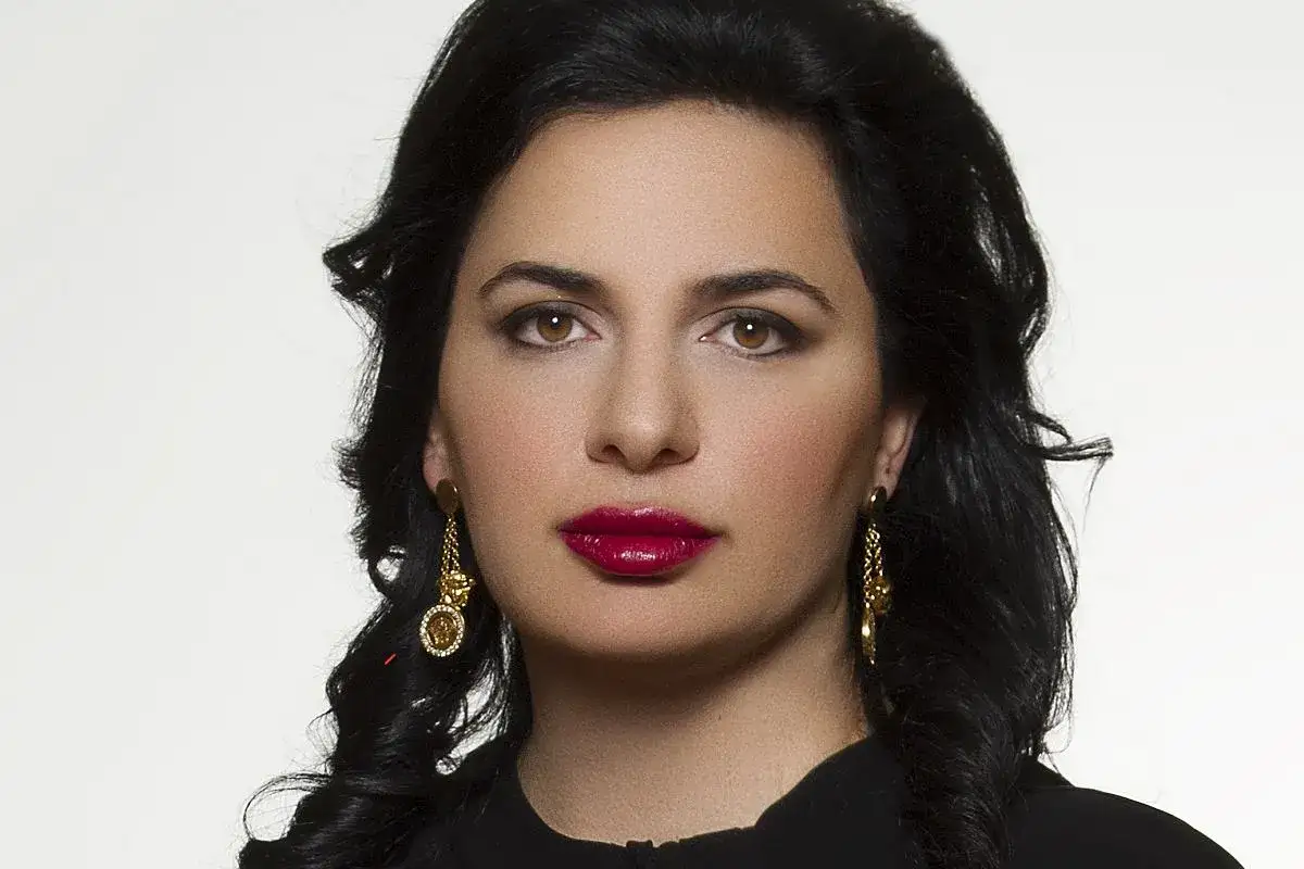 Portret Ruja Ignatova, kobiety o ciemnych włosach i wyrazistych ustach, noszącej złote kolczyki.