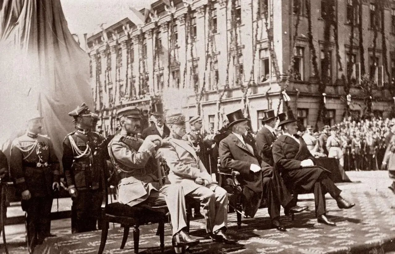 Uroczystość z udziałem wojskowych w mundurach i cywilów w garniturach. W tle budynek ozdobiony girlandami. bbwr.