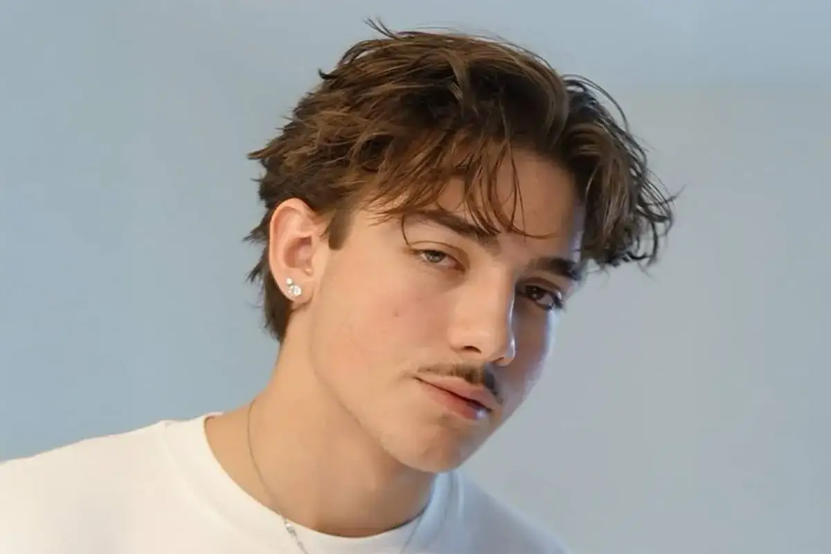 En ung, stilig mittbena kille med en diskret mustasch och en örhänge.