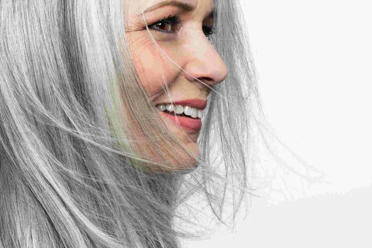 Mujer sonriendo con cabello plateado, mostrando la belleza de porque salen las canas.