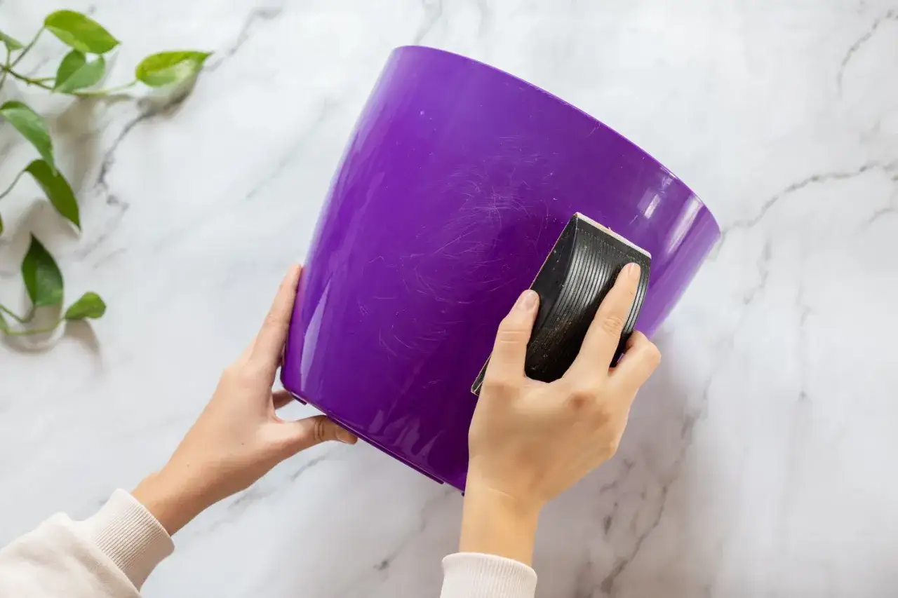 Sanding a purple plastic pot to prepare it for painting. This step is crucial for how to paint acrylic plastic for a smooth finish.