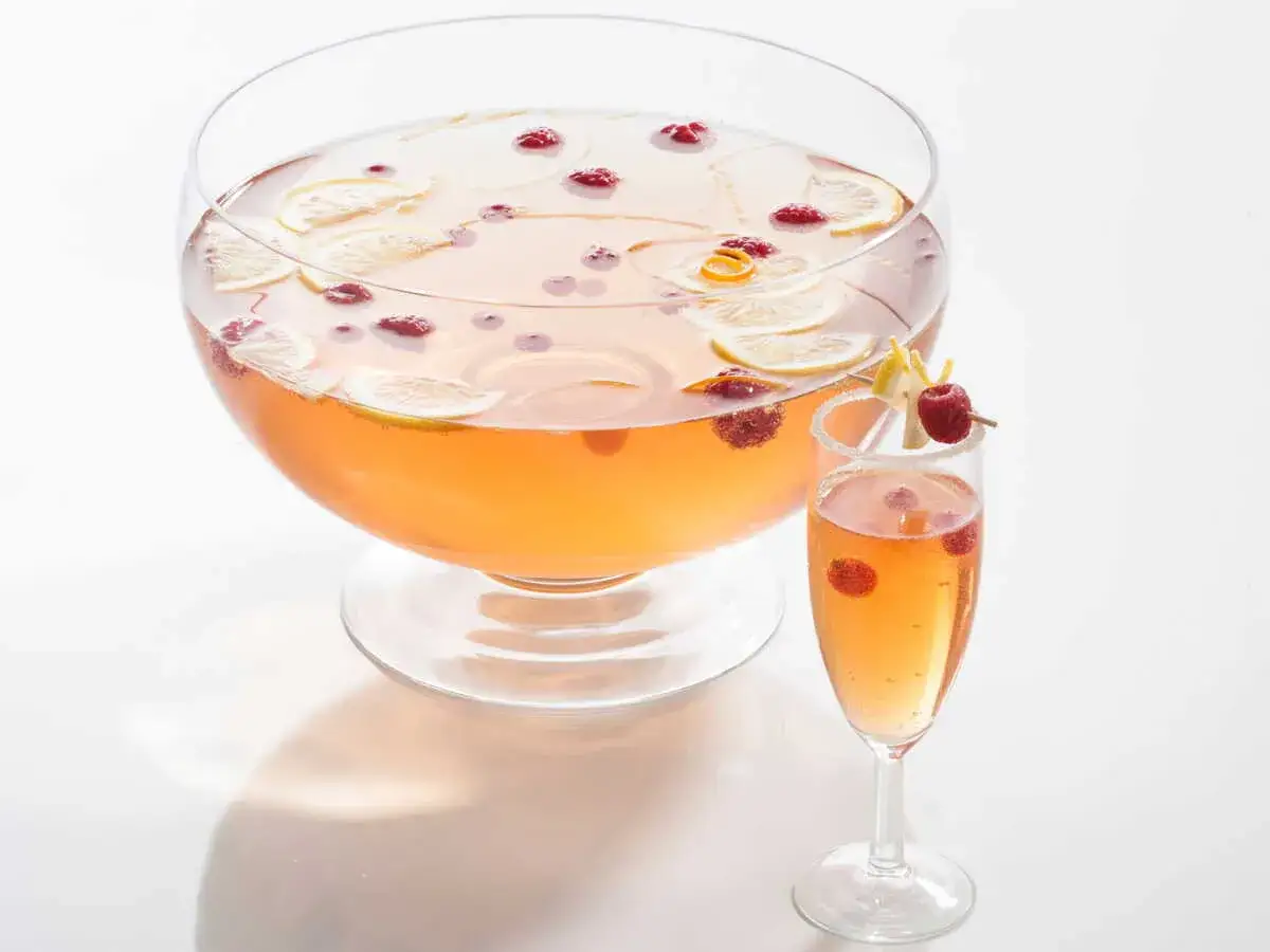 Une coupe de champagne originale, garnie de framboises et de zestes de citron, &agrave; c&ocirc;t&eacute; d'une grande coupe remplie de cette d&eacute;licieuse soupe de champagne.