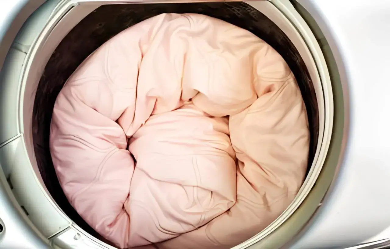 A pink duvet cover is stuffed into a washing machine drum, ready for a wash. Learn how to wash duvet cover for a fresh, clean bed.