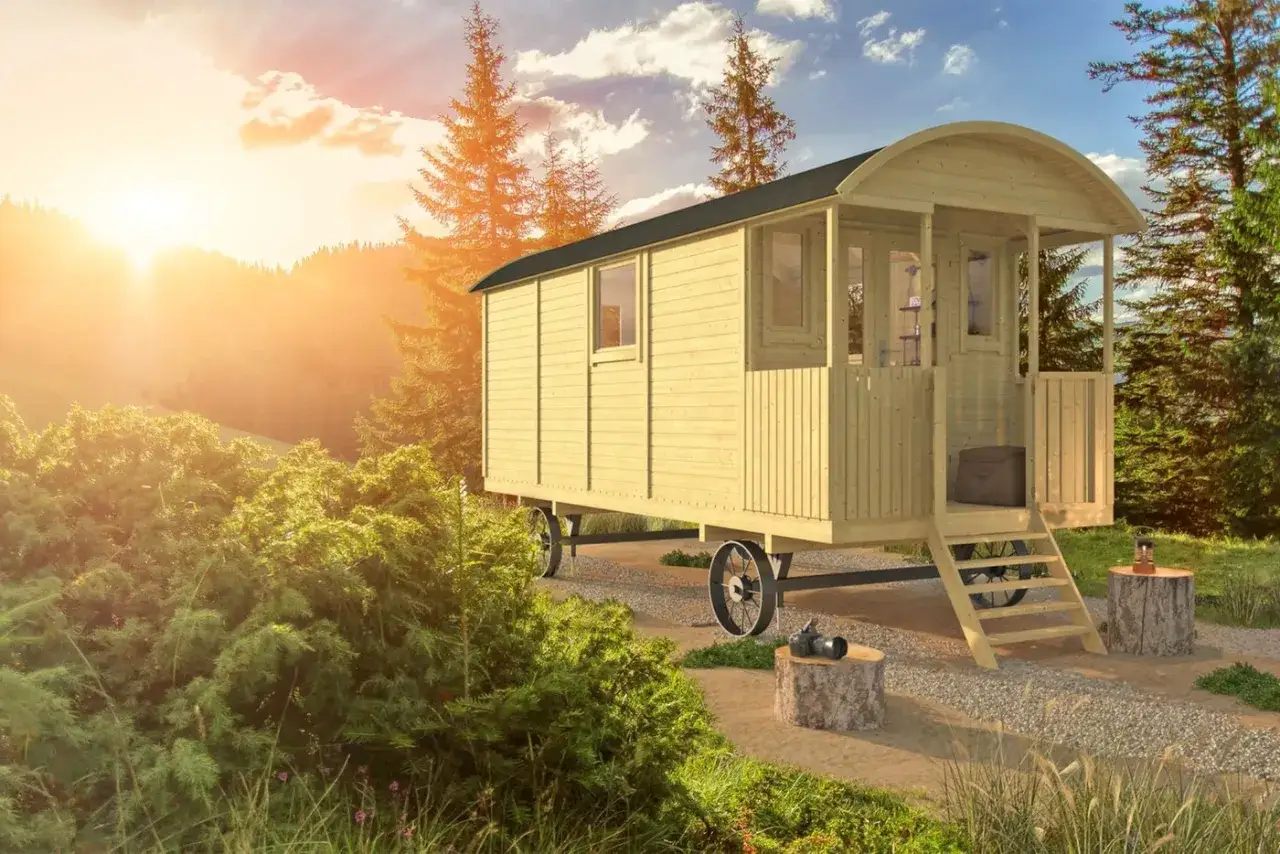 Une caravane transformée en cabane en bois, nichée dans un paysage verdoyant au coucher du soleil. Un refuge pittoresque pour les amoureux de la nature.