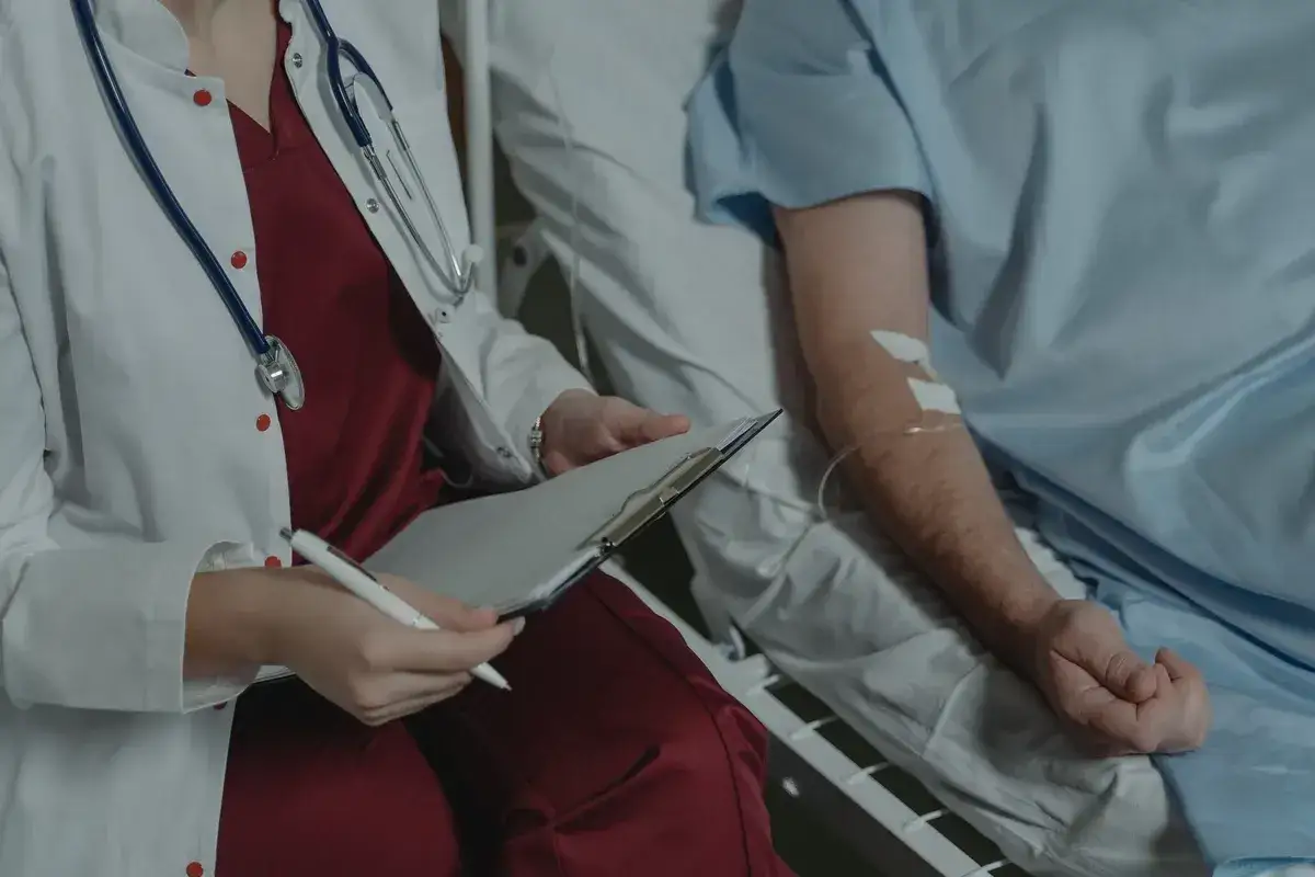 Médecin consultant un dossier près d'un patient sous perfusion, évoquant le parcours difficile du comment meurt-on d'un cancer du pancréas.