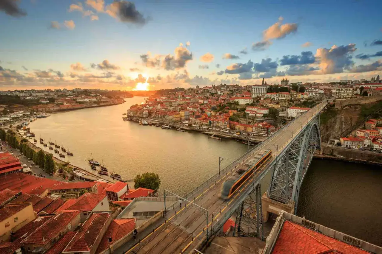 Zachód słońca nad Porto, Portugalia. Listopadowa pogoda sprzyja spacerom po moście, a tramwaj przemierza malowniczą rzekę Douro.