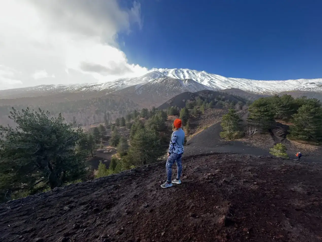 Widok na ośnieżony wulkan Etna, gdzie turystka podziwia krajobraz podczas wejścia na Etnę.