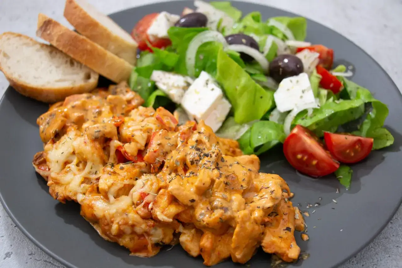 Gegrilltes Hähnchen in cremiger griechischer Metaxasauce, serviert mit Brot und einem frischen Salat mit Feta.