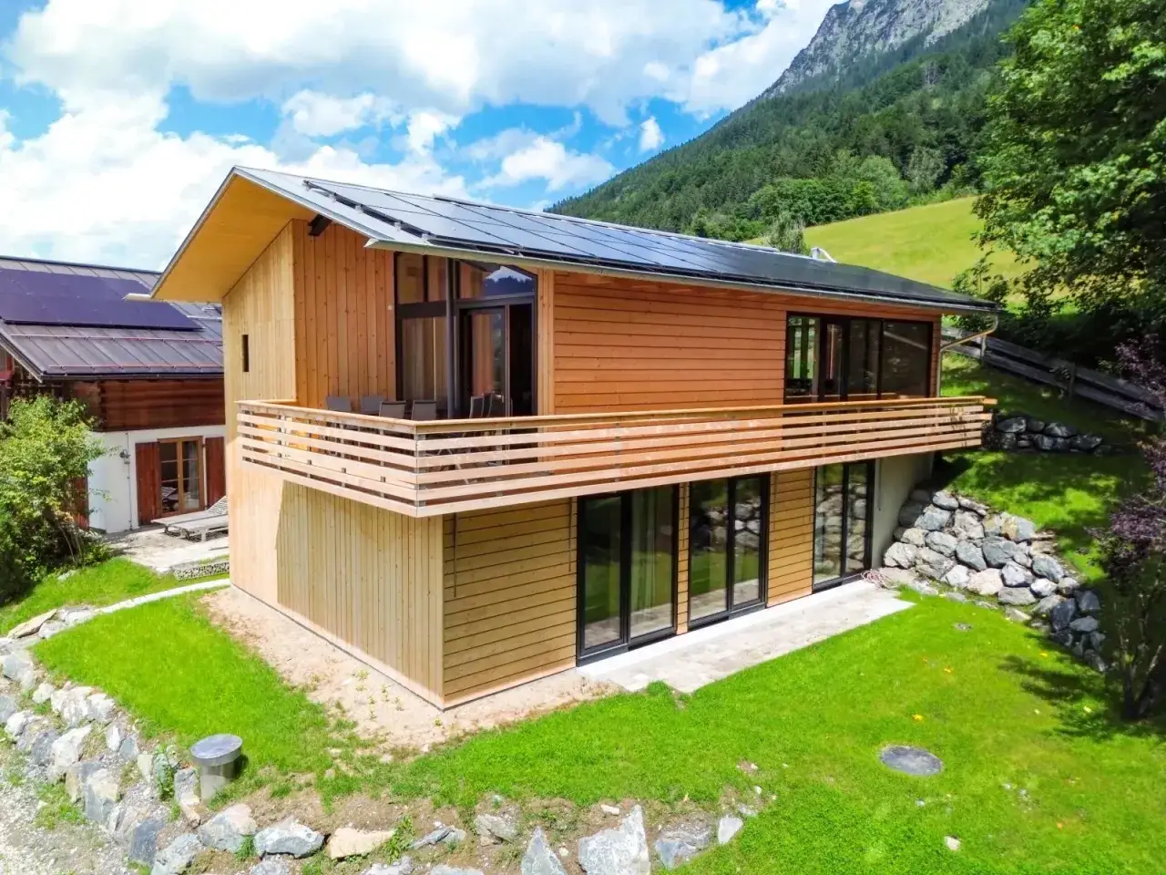 Modernes Holzhaus mit Solaranlage, Balkon und großen Fenstern. Ein Beispiel, was ein Chalet in den Bergen sein kann.