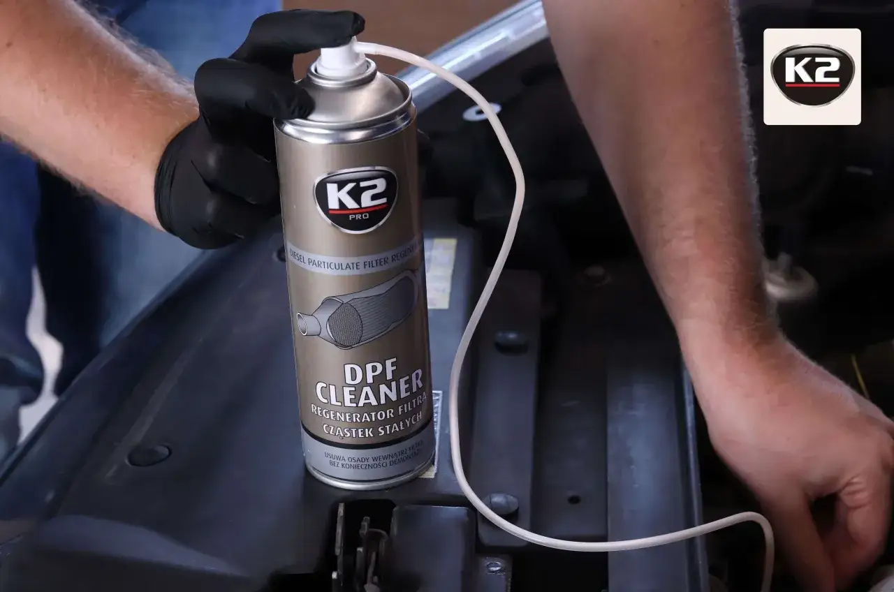 Ręce w czarnych rękawiczkach trzymają puszkę K2 DPF Cleaner, gotową do czyszczenia filtra cząstek stałych.