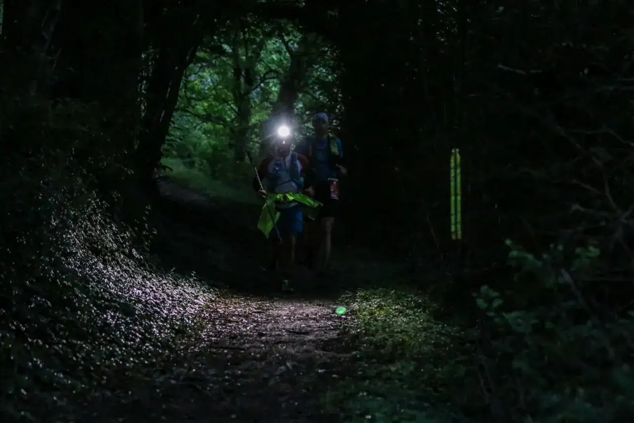 Deux coureurs s'aventurent dans un sentier forestier sombre, leurs lampes frontales &eacute;clairant le chemin. Un choix judicieux de lampe frontale est essentiel pour une telle course.