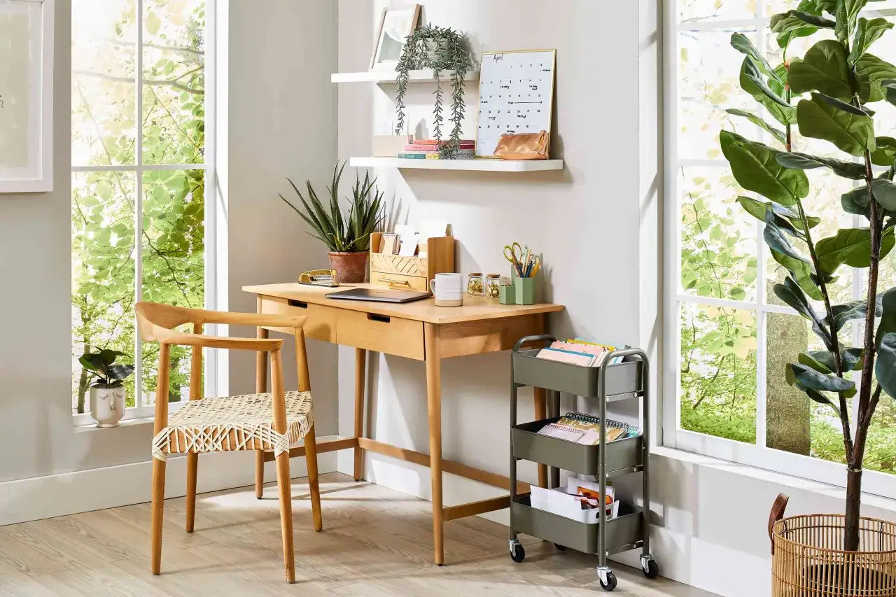 Bright, airy home office with a wooden desk, chair, plants, and a rolling cart. Great small office decor ideas for a productive workspace.