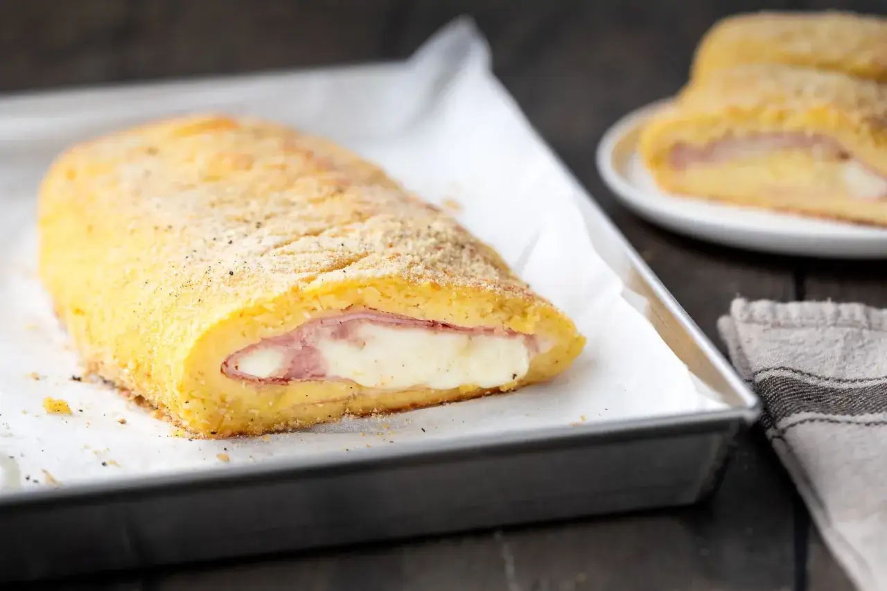 Polpettone di patate ripieno di prosciutto e formaggio filante, cotto al forno e dorato.