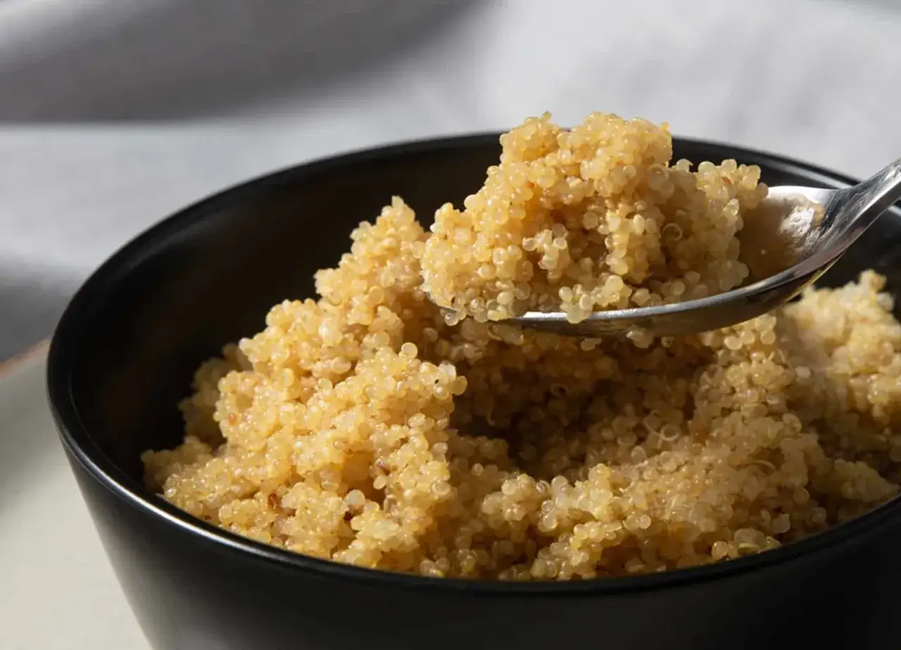 Una ciotola nera piena di quinoa cotta, con un cucchiaio che ne solleva una porzione. Perfetta per imparare come cuocere la quinoa.