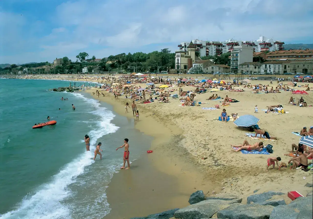 Gente disfrutando de un día soleado en una de las mejores playas de Barcelona, con el mar azul y edificios al fondo.