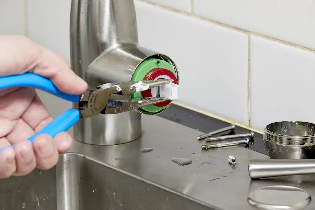 Maintenant, je comprends la dur&eacute;e de vie cartouche mitigeur. Une main utilise une pince pour retirer une pi&egrave;ce blanche d'un robinet.