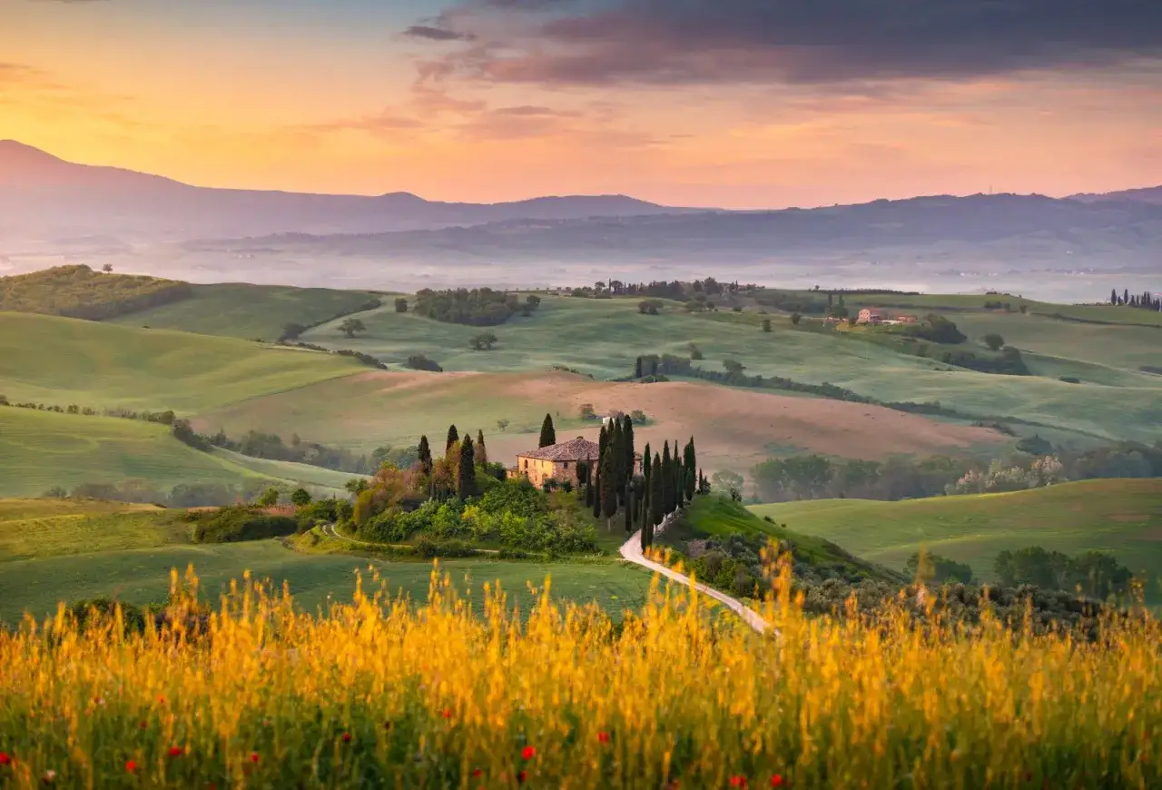 Dolci colline toscane al tramonto, un casale con cipressi. Perfetto per scoprire cosa visitare in Toscana in 1 giorno.