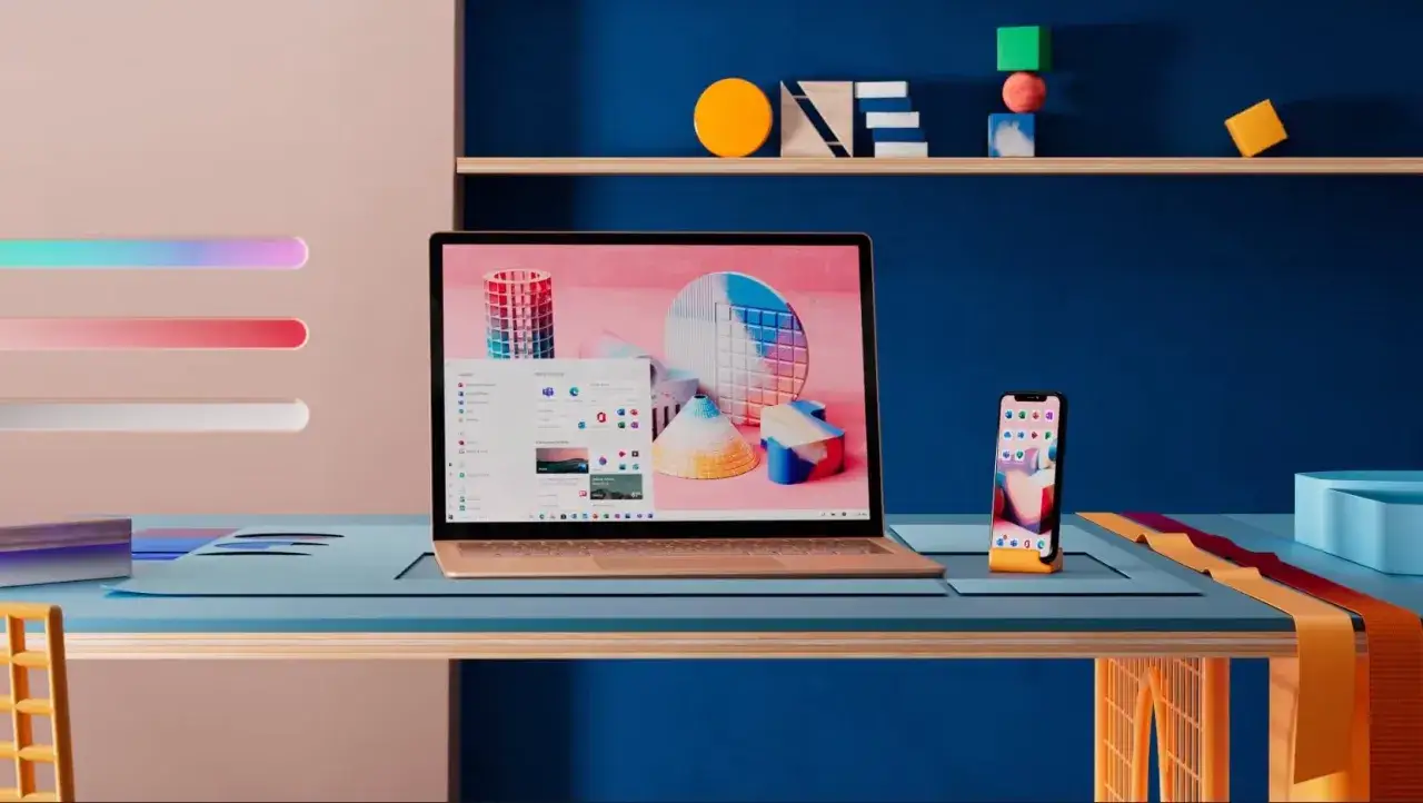 Nowoczesny pulpit z laptopem i telefonem, gotowy na aktualizacja windows 10. Kolorowe akcenty i geometryczne kształty tworzą inspirującą przestrzeń.