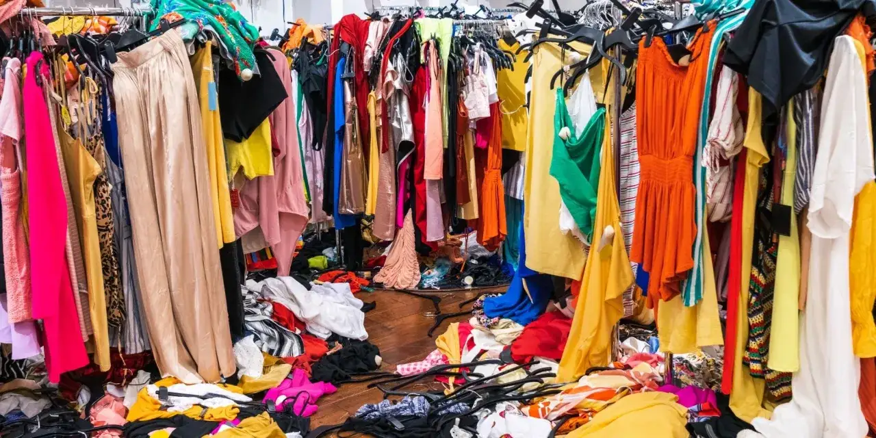 Bunte Kleider auf Kleiderstangen und auf dem Boden. Die Vielfalt zeigt die schnellen **fast fashion vorteile**: ständig neue Trends für jeden Geldbeutel.