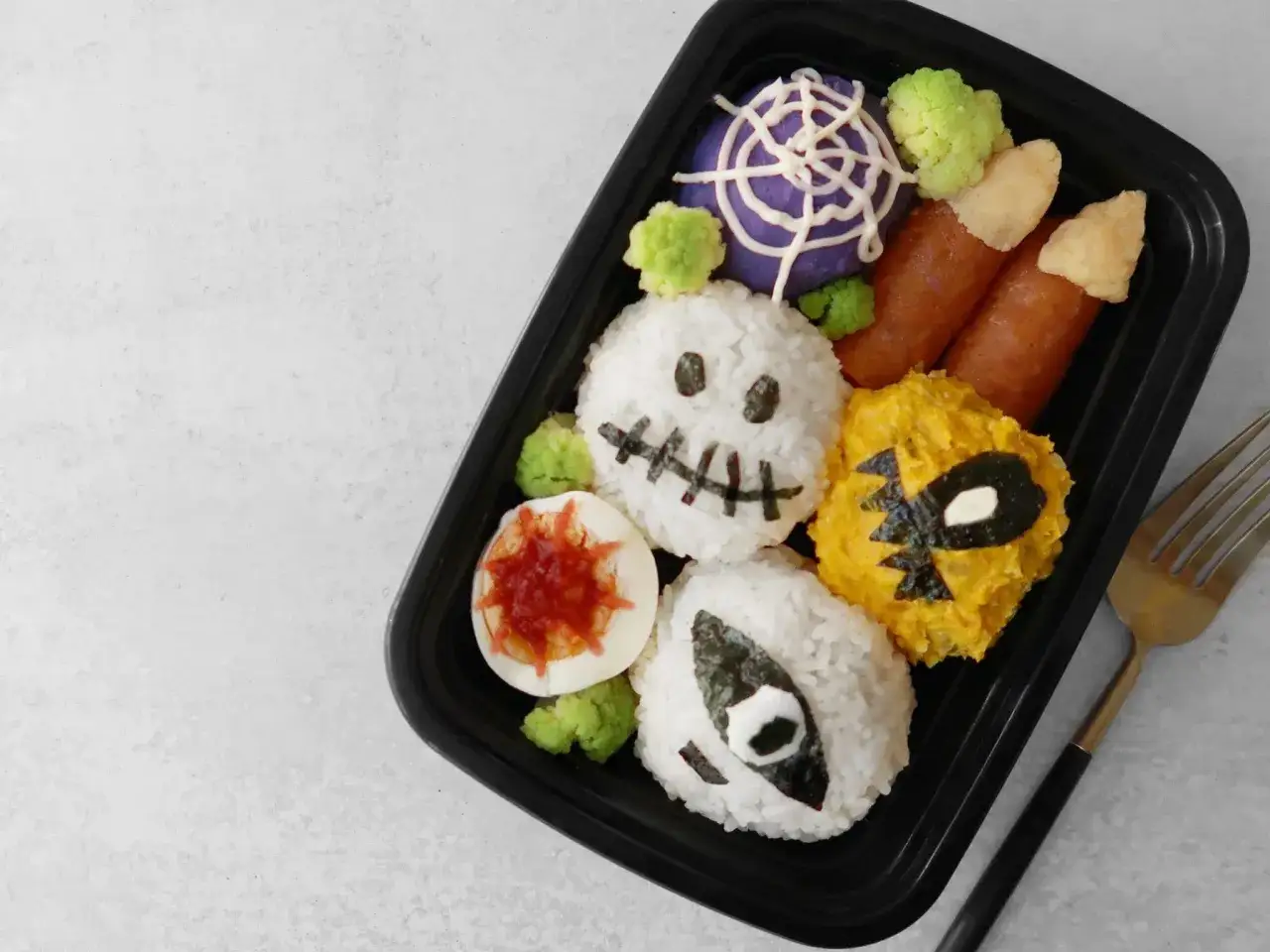 A spooky Halloween bento box filled with rice balls shaped like ghosts and skulls, sausage