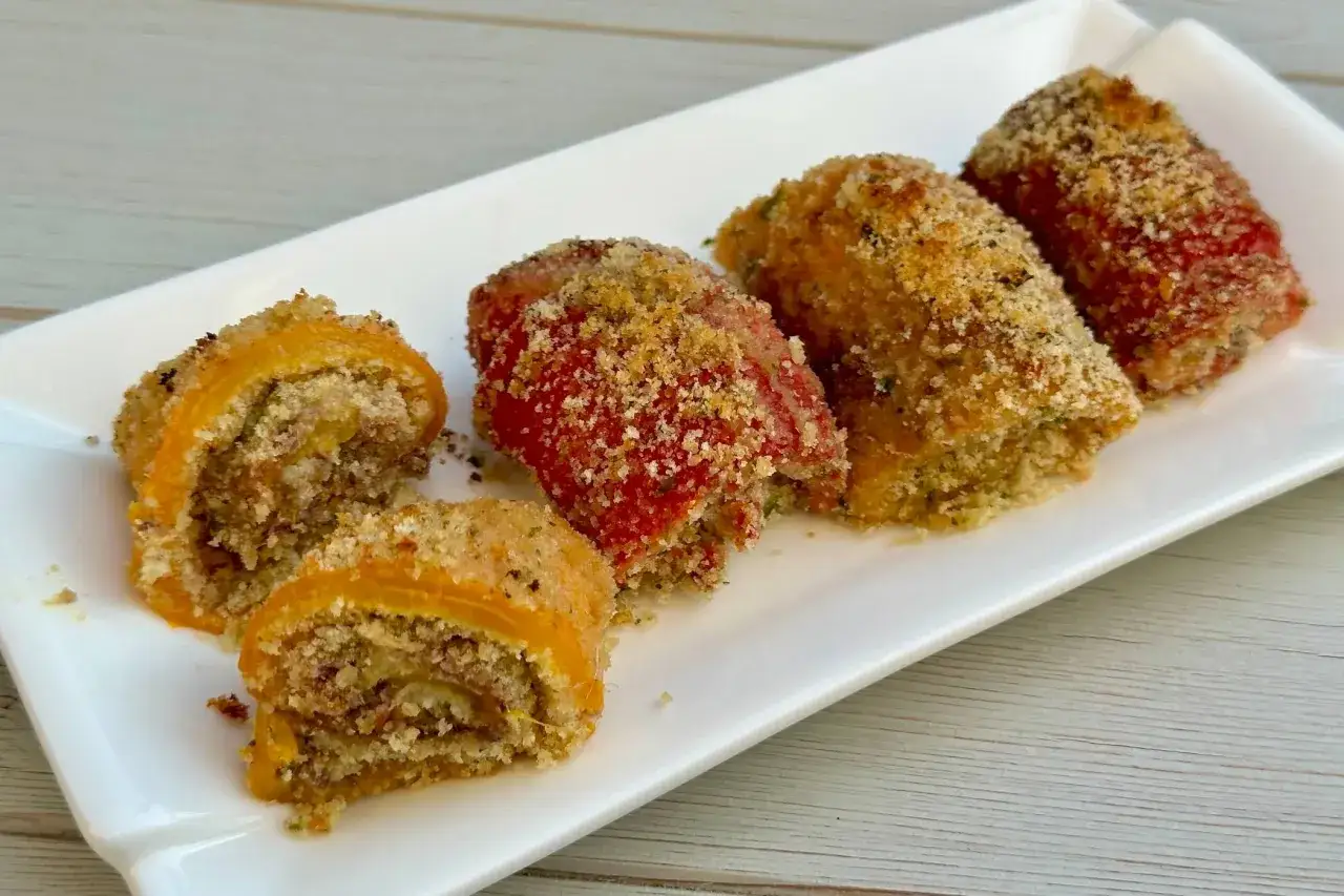 Deliziosi involtini di peperoni ripieni e impanati, serviti su un piatto bianco.