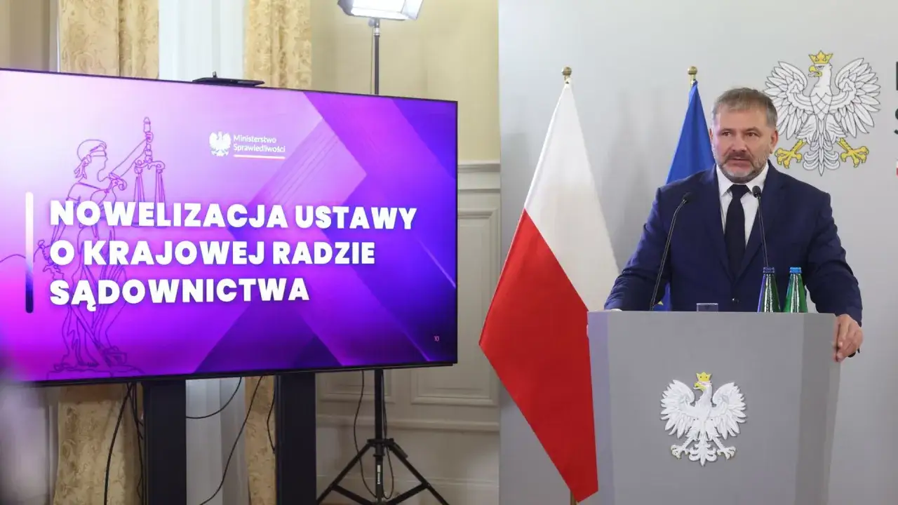 Minister sprawiedliwości przemawia na tle ekranu z napisem