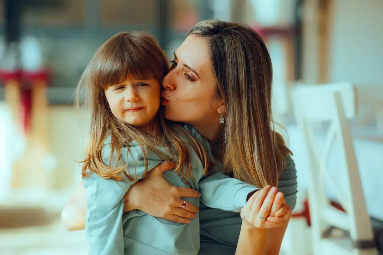 Una madre bacia la sua bambina, che sembra un po' infastidita. I bambini non si baciano, ma l'amore materno &egrave; forte.