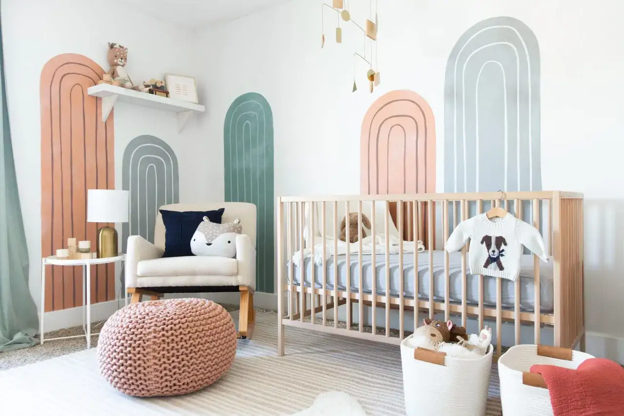 A modern nursery with boho rainbow wall art, a wooden crib, and a comfy armchair. This room showcases sweet nursery themes with its playful decor.