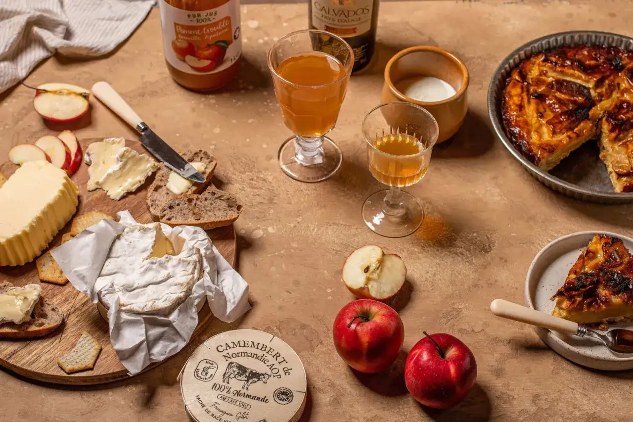 Un plateau de spécialités normandie : camembert, beurre, cidre, jus de pomme et tarte aux pommes.