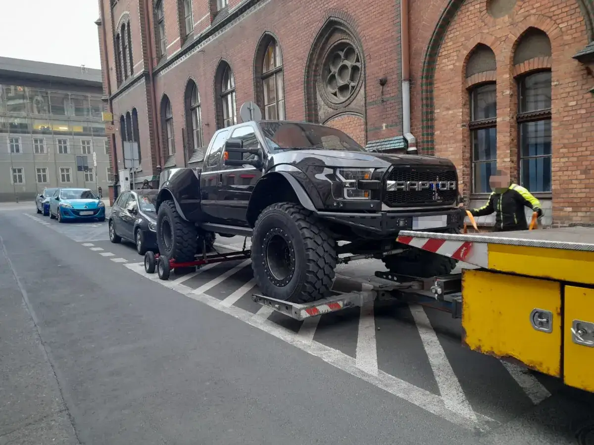 Potężny Ford F350 Raptor na lawecie, gotowy do transportu. Obok stoją inne samochody.