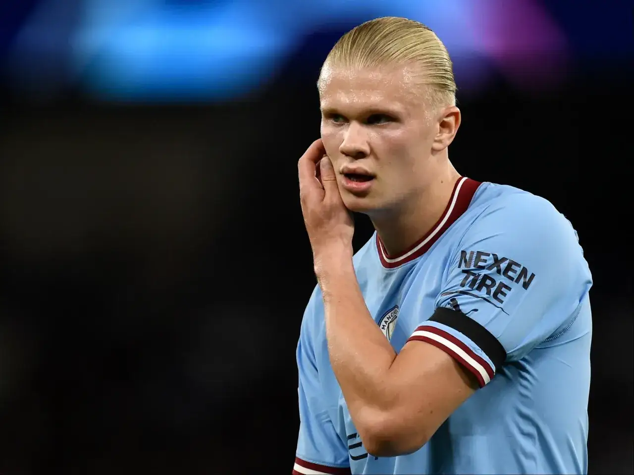 Erling Haaland, w jasnoniebieskiej koszulce z logo Manchesteru City, z dłonią przy uchu, słucha dopingu kibic&oacute;w. To właśnie tam gra Haaland.