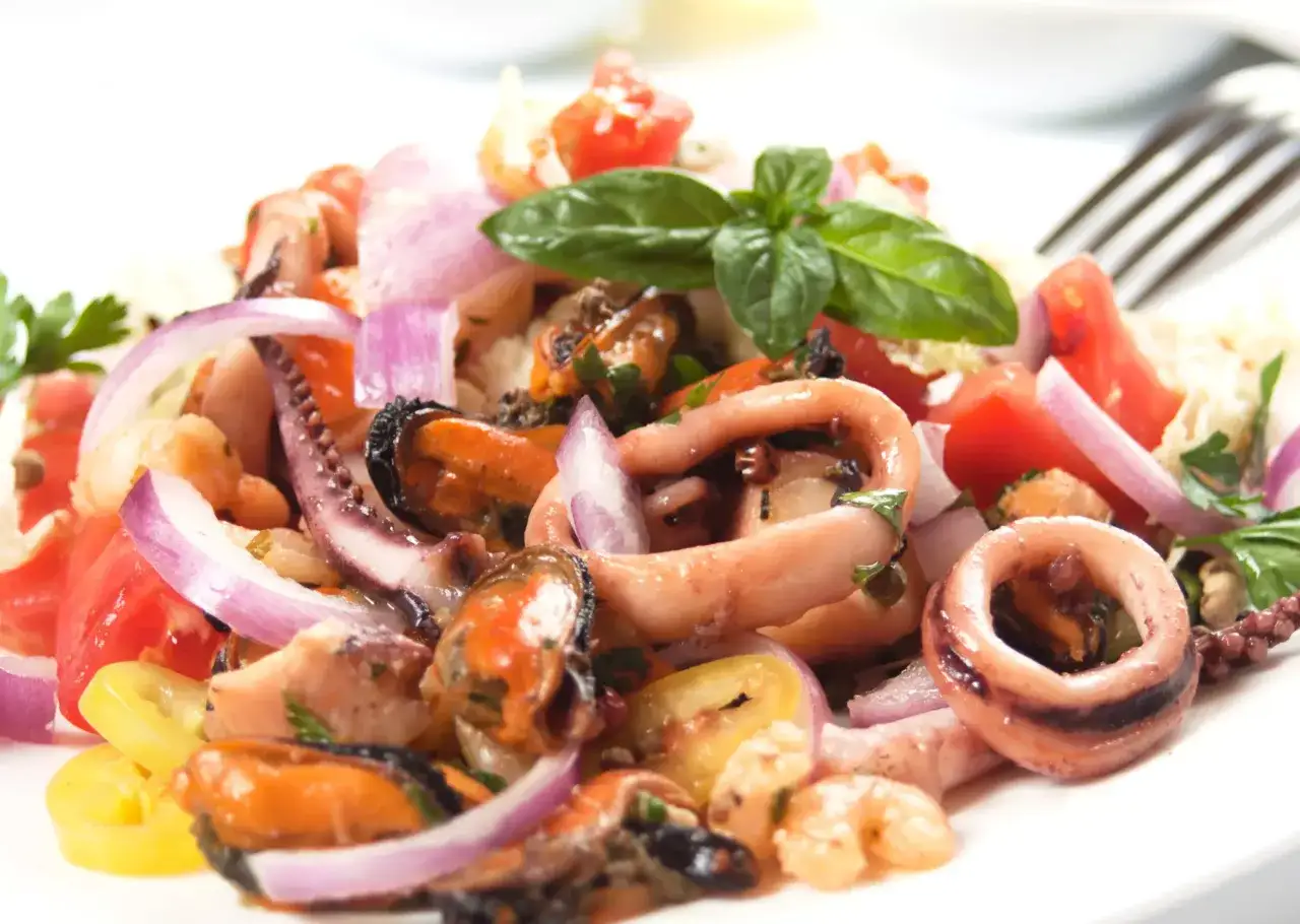 Deliciosa ensalada de marisco con pulpo, calamares, mejillones y gambas, aderezada con cebolla morada, tomate y hierbas frescas.