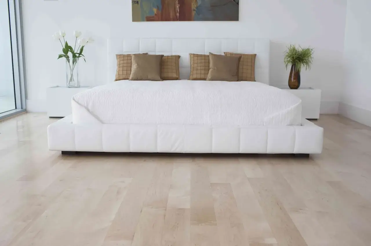 Helles Holz als Bodenbelag im Schlafzimmer, passend zum modernen wei&szlig;en Bett mit Steppung und Kissen.