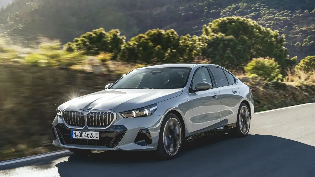 Nowe BMW Serii 5 sunie po krętej drodze wśród zielonych wzgórz.