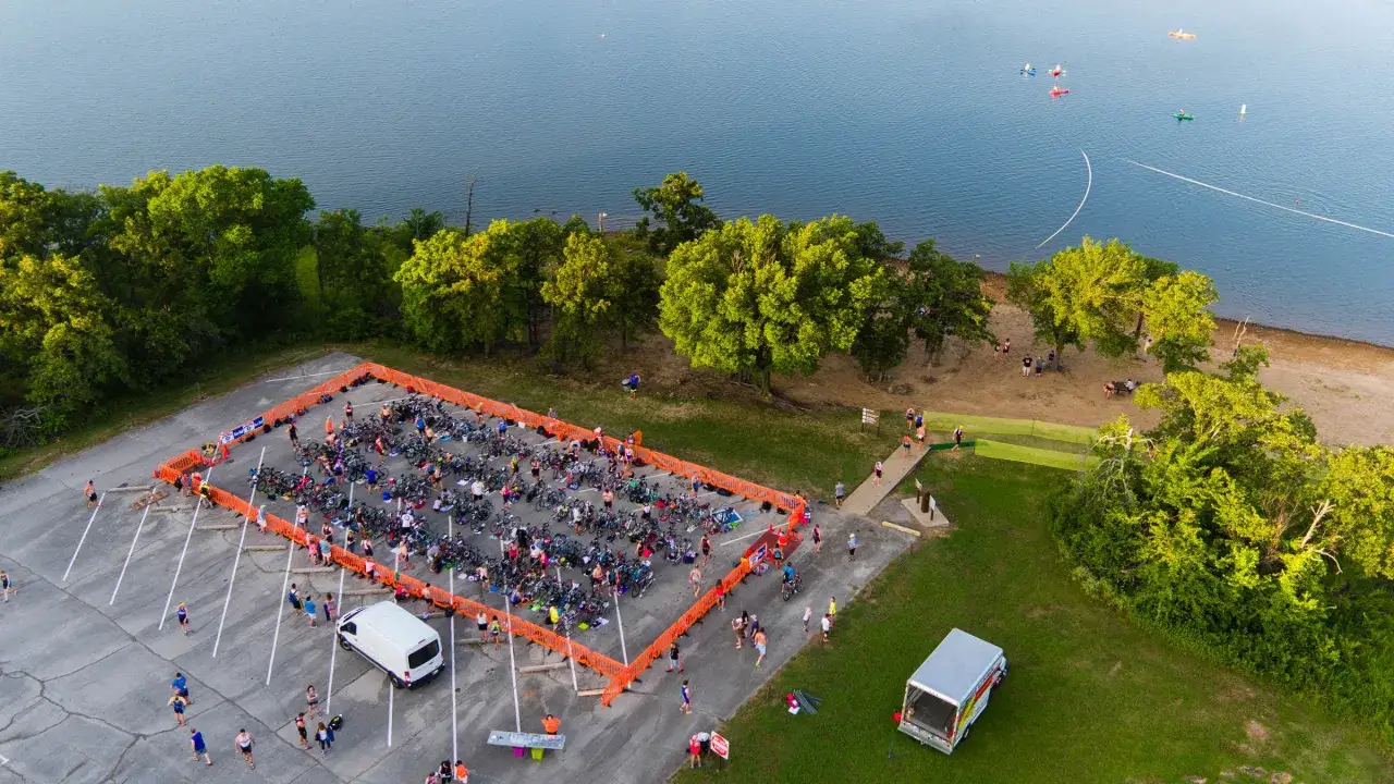 F&ouml;rberedelser inf&ouml;r en triathlon vid en sj&ouml;. M&aring;nga cyklar st&aring;r uppradade i ett avsp&auml;rrat omr&aring;de, redo f&ouml;r t&auml;vlingen. En scen som p&aring;minner om Runners World Triathlon.