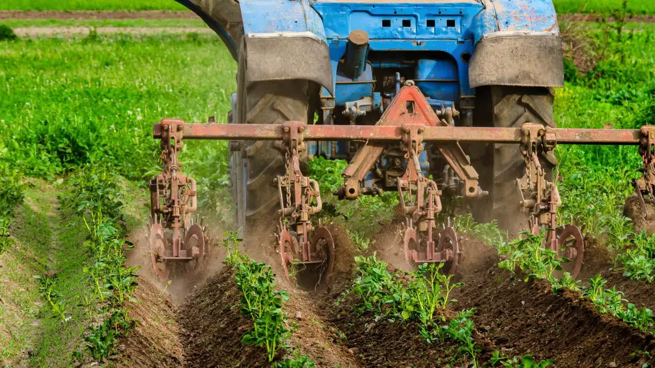 Niebieski traktor z narzędziami uprawia pole, wspierając rolnictwo regeneratywne.