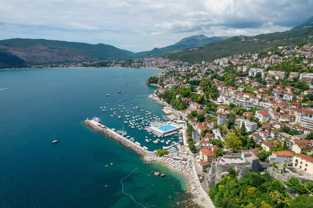 Widok z lotu ptaka na malownicze miasta w Czarnog&oacute;rze, z zatoką pełną łodzi, plażą i starożytną twierdzą.