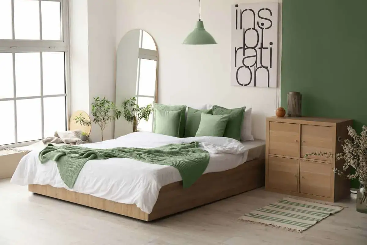 Habitaci&oacute;n moderna con cama, espejo, plantas y un cuadro de inspiraci&oacute;n. Una pared verde da ideas sobre como pintar una habitacion.