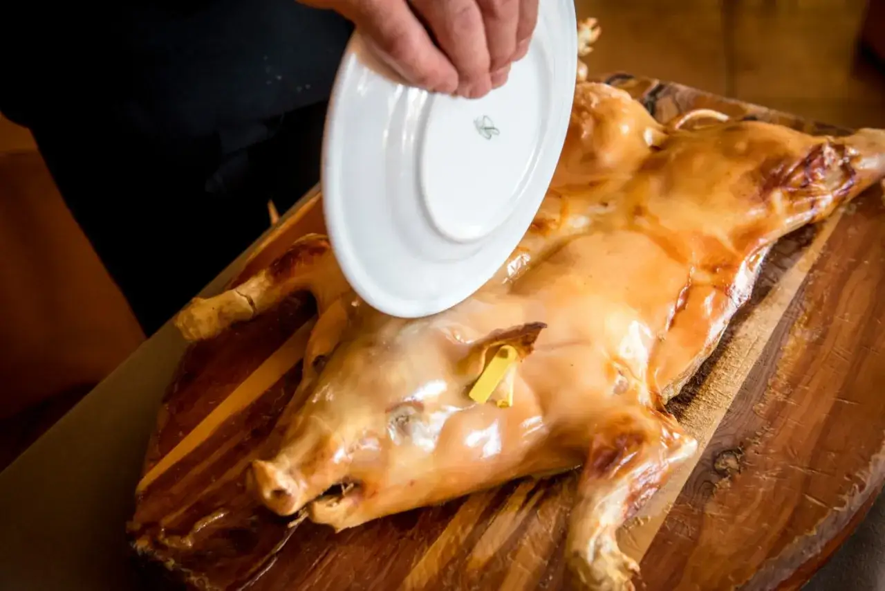 Un chef presenta un cochinillo asado segoviano, crujiente y dorado, listo para ser servido.