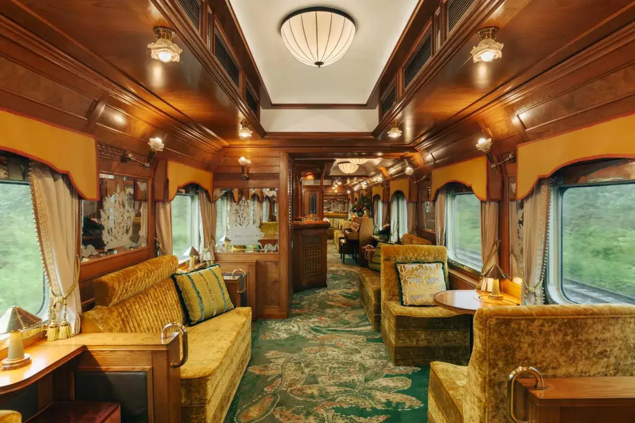 Lussuoso vagone del **percorso Orient Express**, con divani in velluto ocra, tappeti fiorati e boiserie in legno.