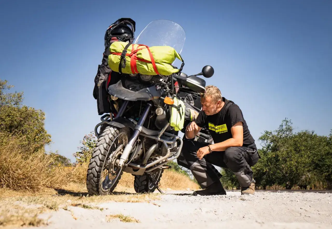 Mężczyzna sprawdza, co zabrać na wyprawę motocyklową. Motocykl załadowany bagażem, kask i zielona torba podróżna.