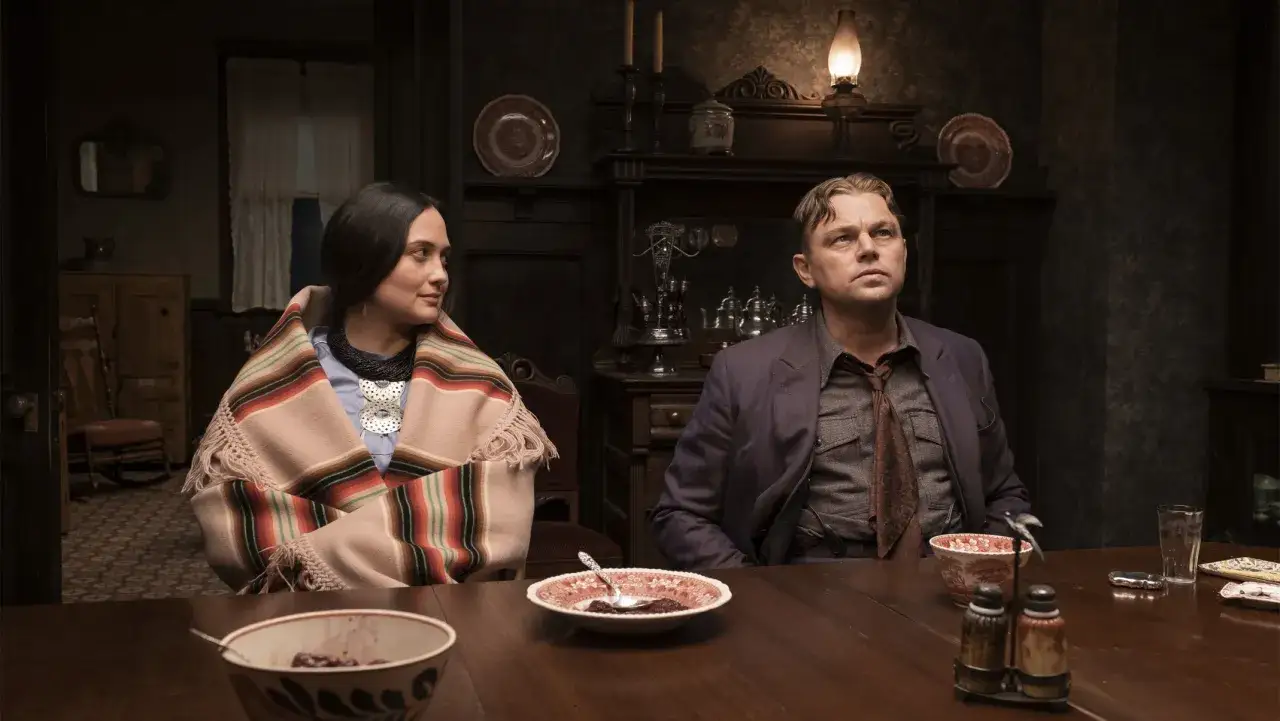 En kvinna i en traditionell filt och en man sitter vid ett bord. En scen från
