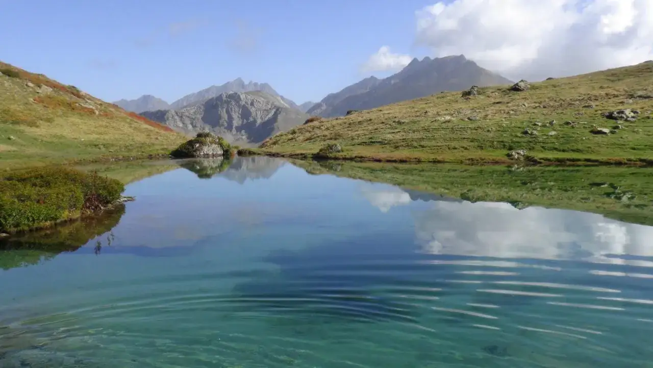Un sereno ib&oacute;n de espelunciecha refleja monta&ntilde;as y un cielo azul con nubes.