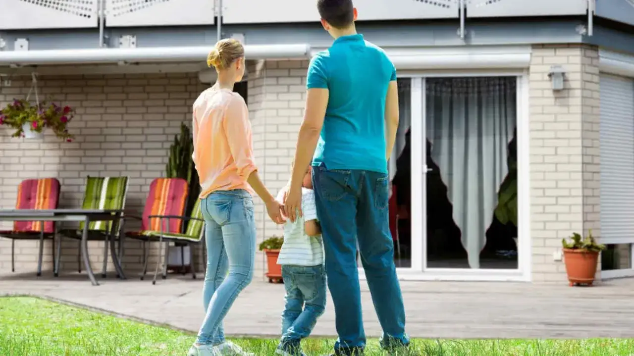 Ein Ehepaar mit Kind vor ihrem neuen Haus. Sie überlegen, wie sie ihr unterschiedliches Eigenkapital für den Hauskauf am besten einsetzen.