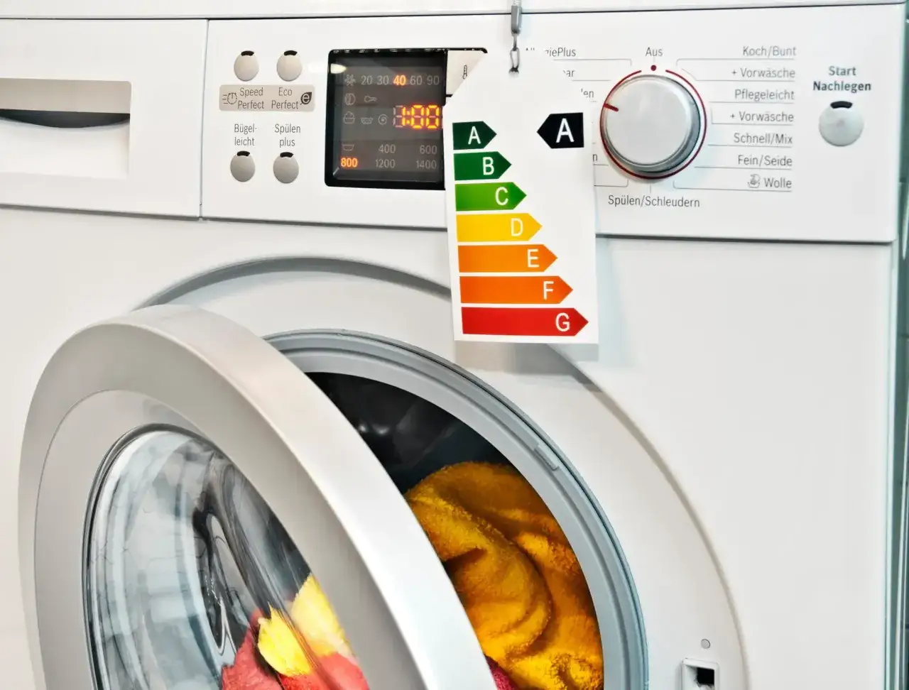 Eine moderne, pflegeleicht Waschmaschine mit Energieeffizienzlabel A. Die T&uuml;r ist ge&ouml;ffnet und bunte W&auml;sche ist sichtbar.